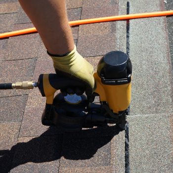 New roof shingle being applied. A Roofer nailing asphalt shingles with air gun.