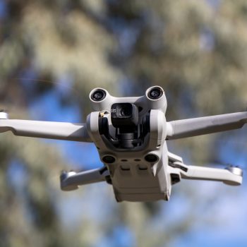 Close up drone with camera sensors and props flying in air with nature behind - DJI Mini 3 Pro aerial uav