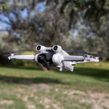 Close up drone with camera sensors and props flying in air with nature behind - DJI Mini 3 Pro aerial uav